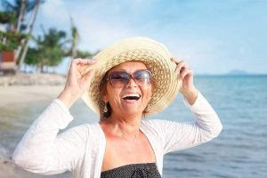 A woman smiling and holding her hat on the beach